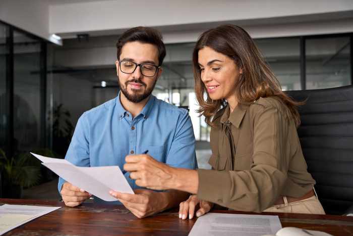 Dos profesionales egresados de la especialidad en recursos humanos, sosteniendo documentos en las manos, revisan los resultados de una evaluación de clima laboral.