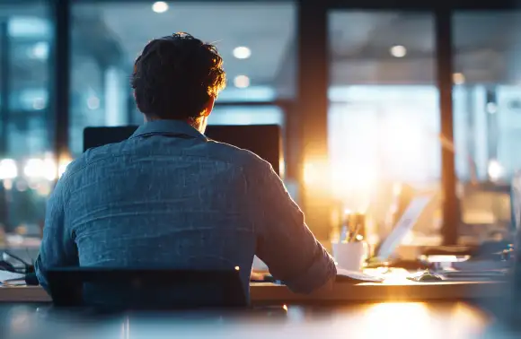 Profesional observando con determinación desde su escritorio, símbolo de innovación empresarial y visión estratégica en entornos corporativos.