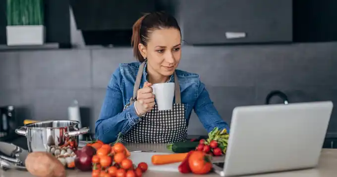Mujer profesional toma curso en línea en su computadora desde la cocina con alimentos saludables