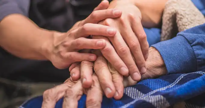 Una persona sostiene las manos de una persona mayor