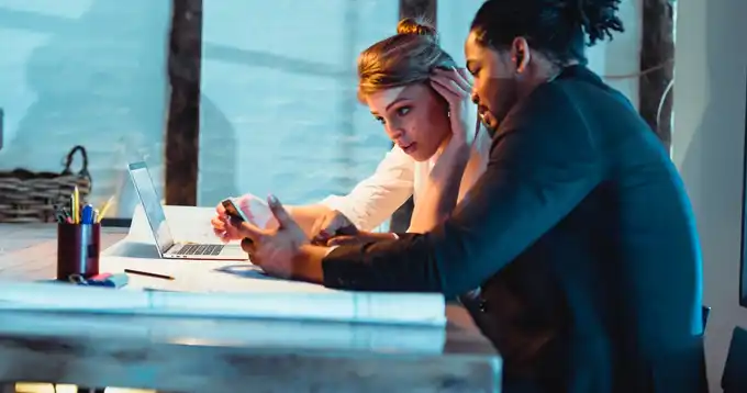 Dos personas sentadas en una mesa con una computadora portátil, trabajando en datos.
