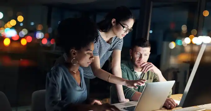 Tres personas trabajando en una laptop en una habitación oscura.