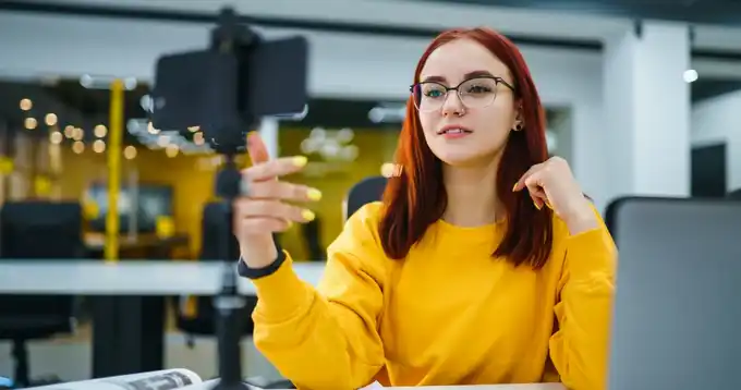 Una joven mujer con gafas toma una clase desde su teléfono móvil.