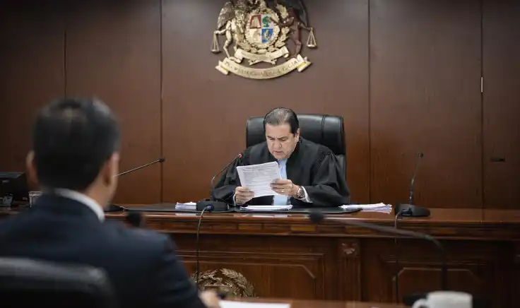 Un mazo de juez de madera sobre una base redonda junto a pequeñas figuras de personas sobre una bandera de Perú, argumentando los cambios en el código penal y litigios en el sistema judicial peruano.