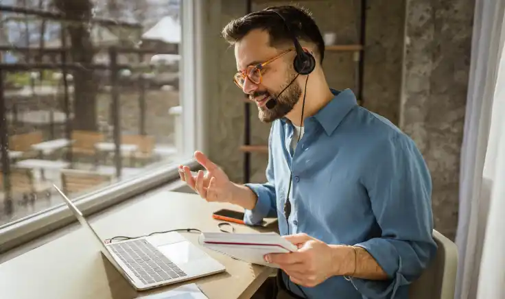 Docente utiliza auriculares con micrófono durante una sesión en línea, representando el uso de tecnología educativa para la enseñanza virtual. 